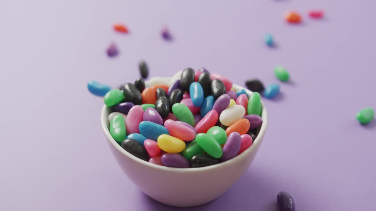 video de primer plano de dulces multicolores que caen en un cuenco sobre un fondo púrpura