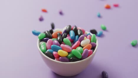 Video-of-close-up-of-multi-coloured-sweets-falling-into-bowl-over-purple-background