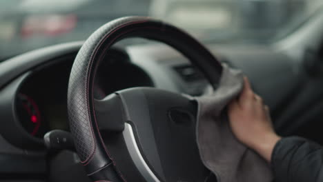 hands of car enthusiast cleaning steering wheel with microfiber cloth in circular motion inside modern car interior, detail shot showing quilted seat cover and dashboard blur, in bright daylight
