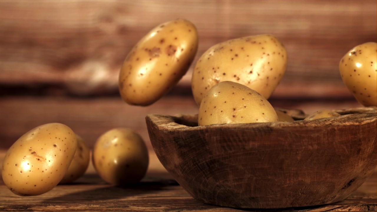 Patate crude che cadono in una ciotola di legno rustica al rallentatore