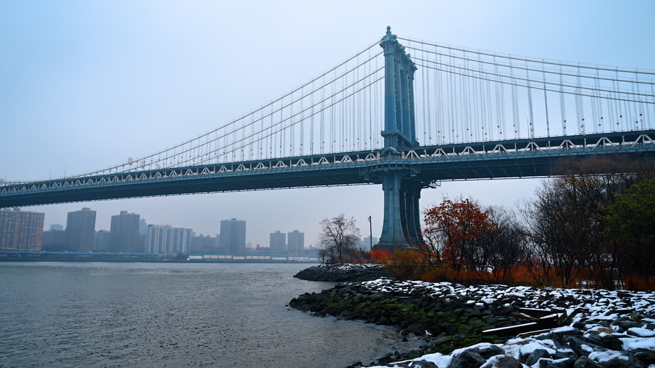 Vista laterale invernale del Manhattan Bridge dal fiume. Vista laterale del Manhattan Bridge sopra l'East River con costa innevata a New York