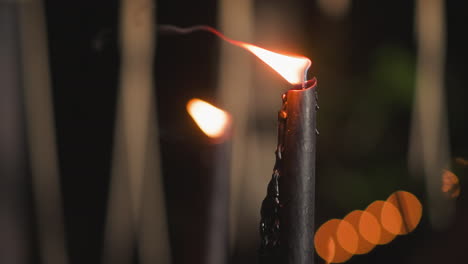 close-up of a burning black candle with blurred lights in the background