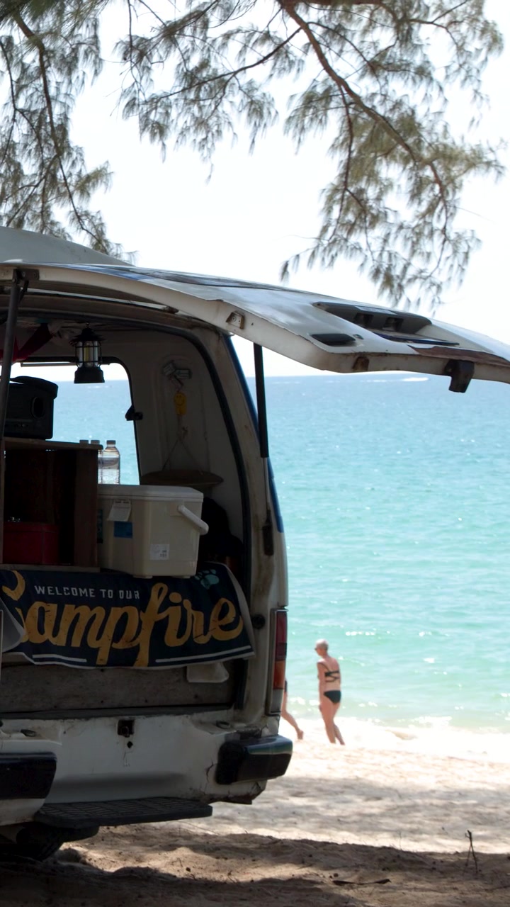 Un camper bianco è parcheggiato su una spiaggia sabbiosa che si affaccia su acque oceaniche turchesi