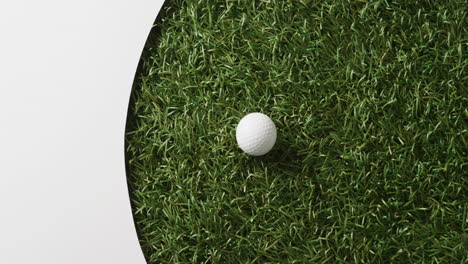 close up of golf ball on grass with white background, copy space, slow motion
