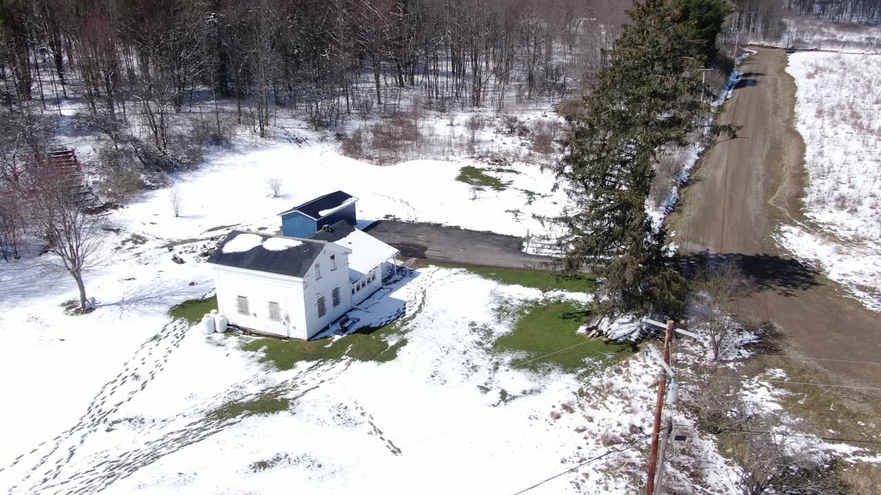 imágenes aéreas de drones que orbitan alrededor de una vieja casa blanca al borde de un bosque, cubierta de nieve
