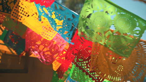 traditional mexican papel picado decorations with intricate designs and vibrant colors, static closeup with sunlight on windy day