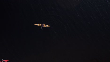 rising drone shot of two kayakers floating on dark murky water