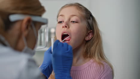 Pediatrician taking child swab test in clinic closeup. Cute child opening mouth