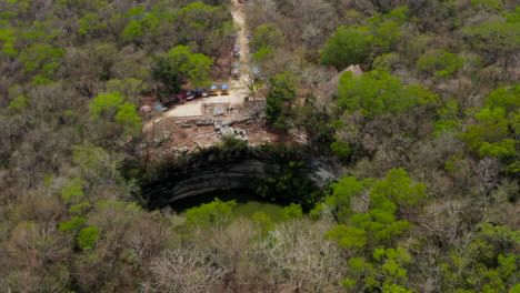 Forwards-tilt-down-reveal-of-large-round-sinkhole-in-ground.-Sun-reflecting-on-water-surface.-Historical-monuments-of-pre-Columbian-era,-Chichen-Itza,-Mexico.