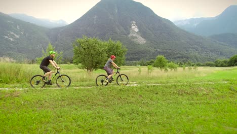 aerial view of a couple driving mountain bikes on dirt road surrounded by hills.