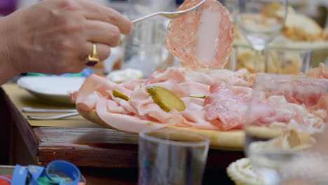 close up of woman hand wearing gold ring picking up food from fresh cold cuts plate