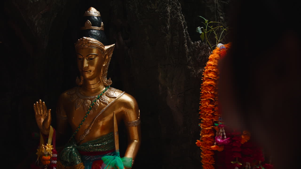 Estátua dourada de Buda em caverna com guirlandas coloridas