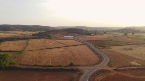 Toma-Aérea-De-Un-Dron-De-Una-Carretera-De-Aldea-Que-Pasa-Por-Granjas-Y-Campos-De-Cultivo-En-Madhya-Pradesh,-India