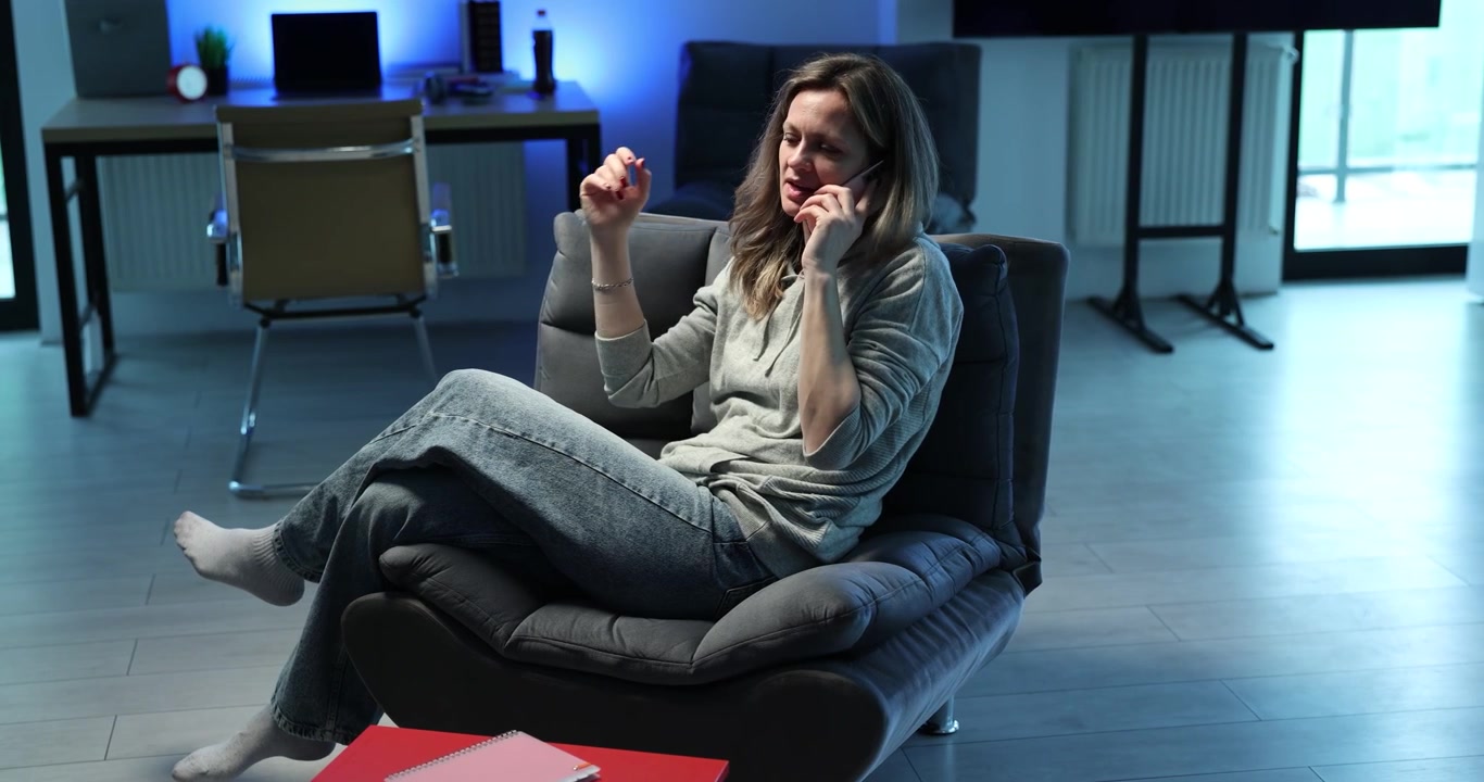 Una donna è seduta in poltrona, impegnata in una conversazione telefonica.