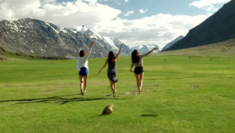 group of friends hold hands and run away from camera toward mountain