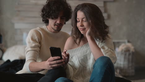 young cute couple in bed looking something funny on the phone and laughing