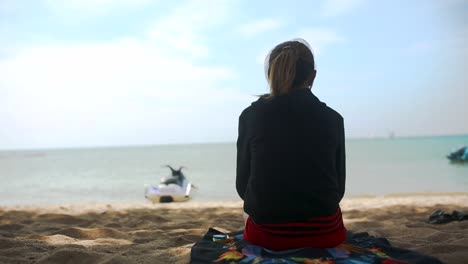 mujer relajándose en la playa, viendo jet ski