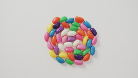 video of overhead view of multi coloured sweets forming circle over white background