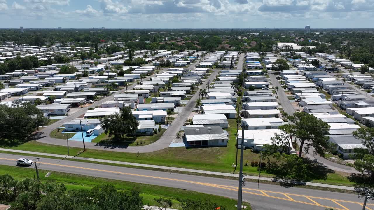 Aerial flyover shot of mobile trailer park with low housing homes in suburb of Cortez, Florida. Sunny day with tropical palm trees in yard. Wide shot.