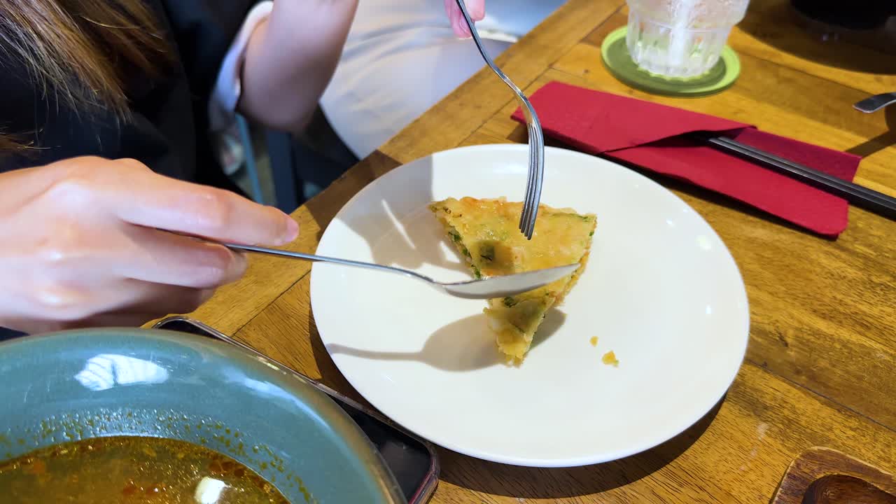 Hands slicing a crispy Vietnamese shrimp pancake on a wooden table in a well-lit restaurant setting
