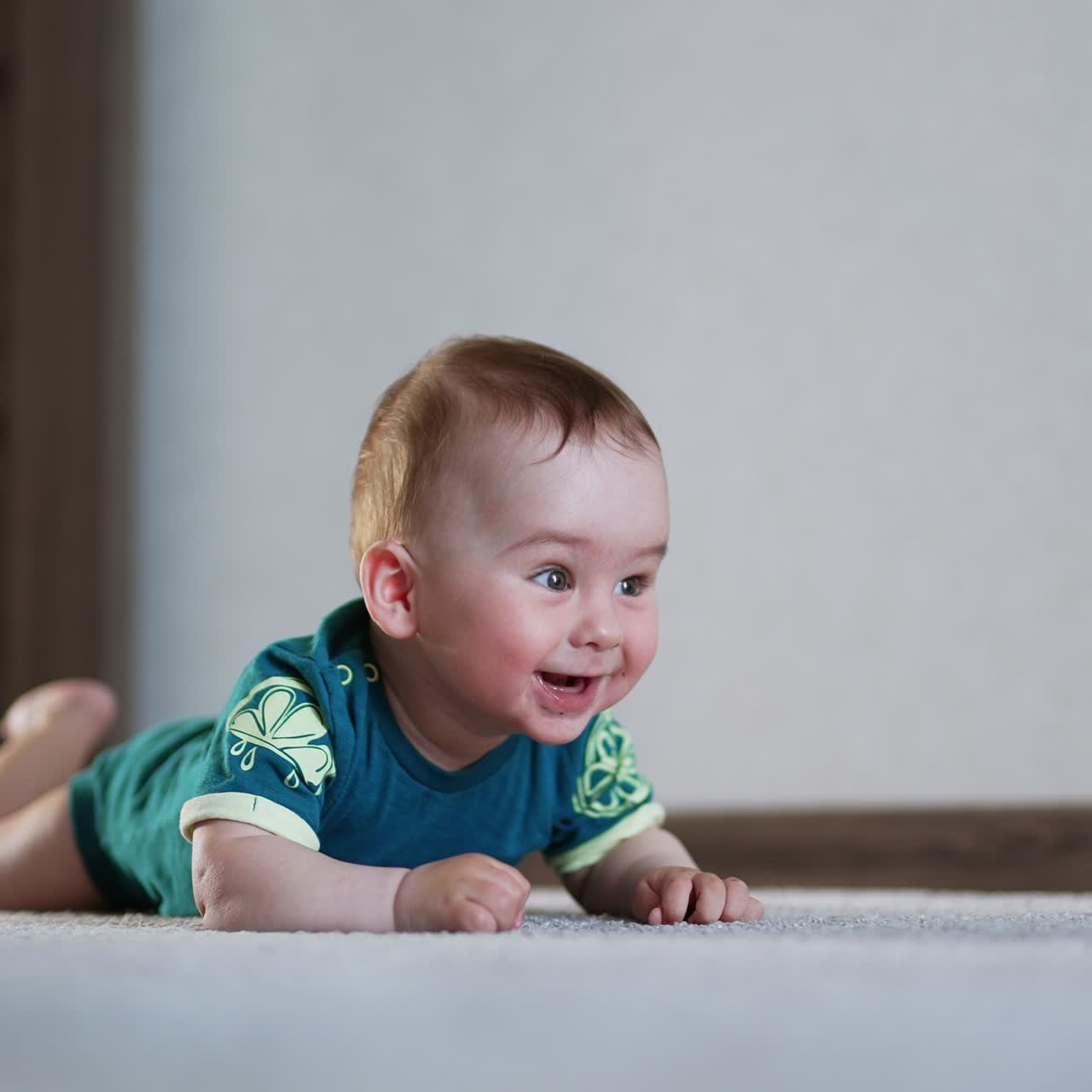 Amazing lovely kid lies still on the floor looking surprised. Nice boy starts to bang his hands and legs by the floor actively
