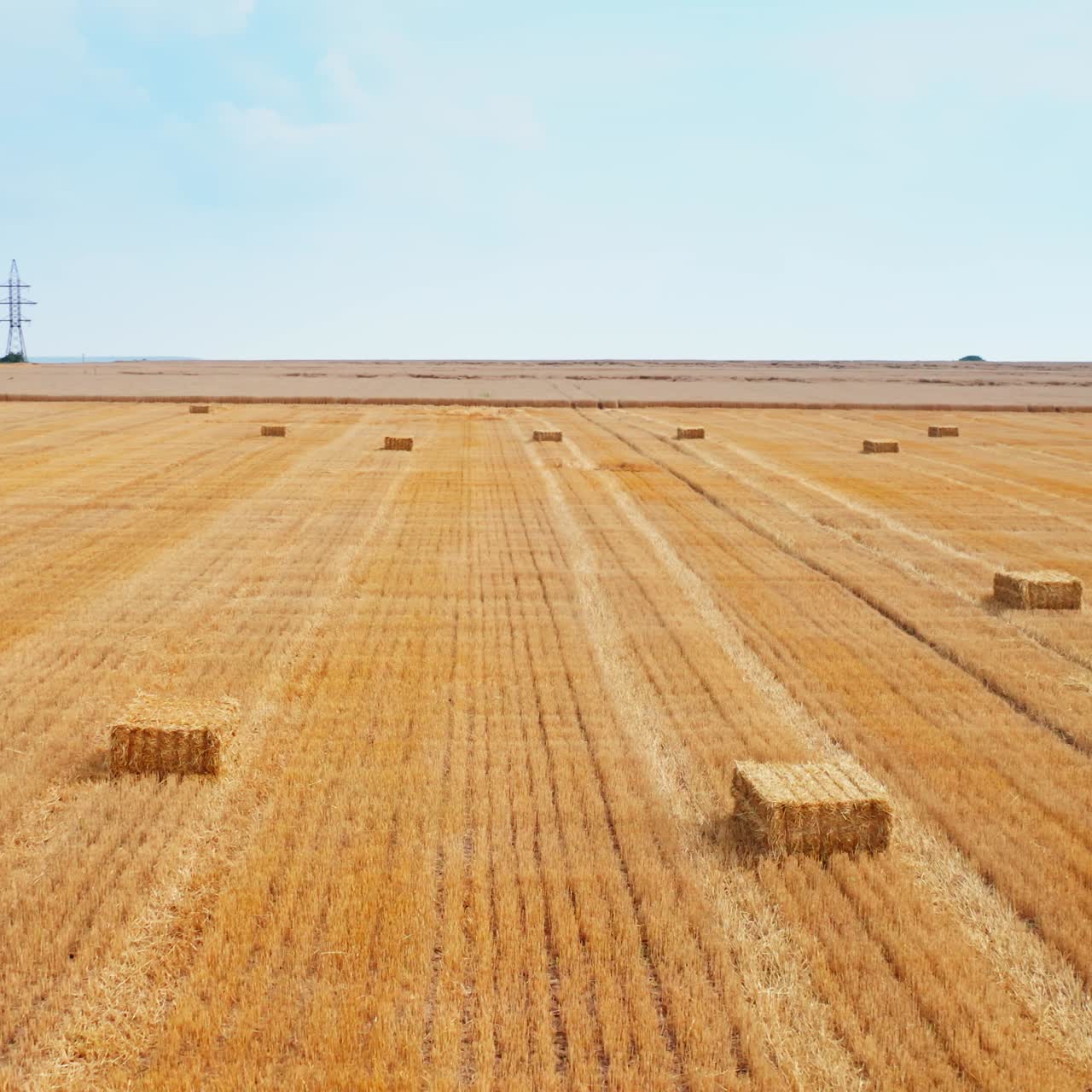 Dry wheat field after harvesting. Circle over the farmland full of hay bales. Agricultural machinery at the backdrop