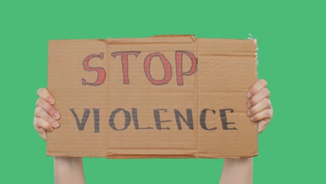 hands holding cardboard with stop violence sign on green chromakey background. hands showing inscription stop violence on green screen background.