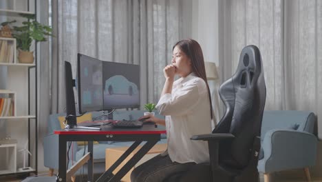 vista lateral de la diseñadora automotriz asiática bostezando mientras trabaja en el modelo 3d del coche ev en las computadoras de escritorio en el estudio