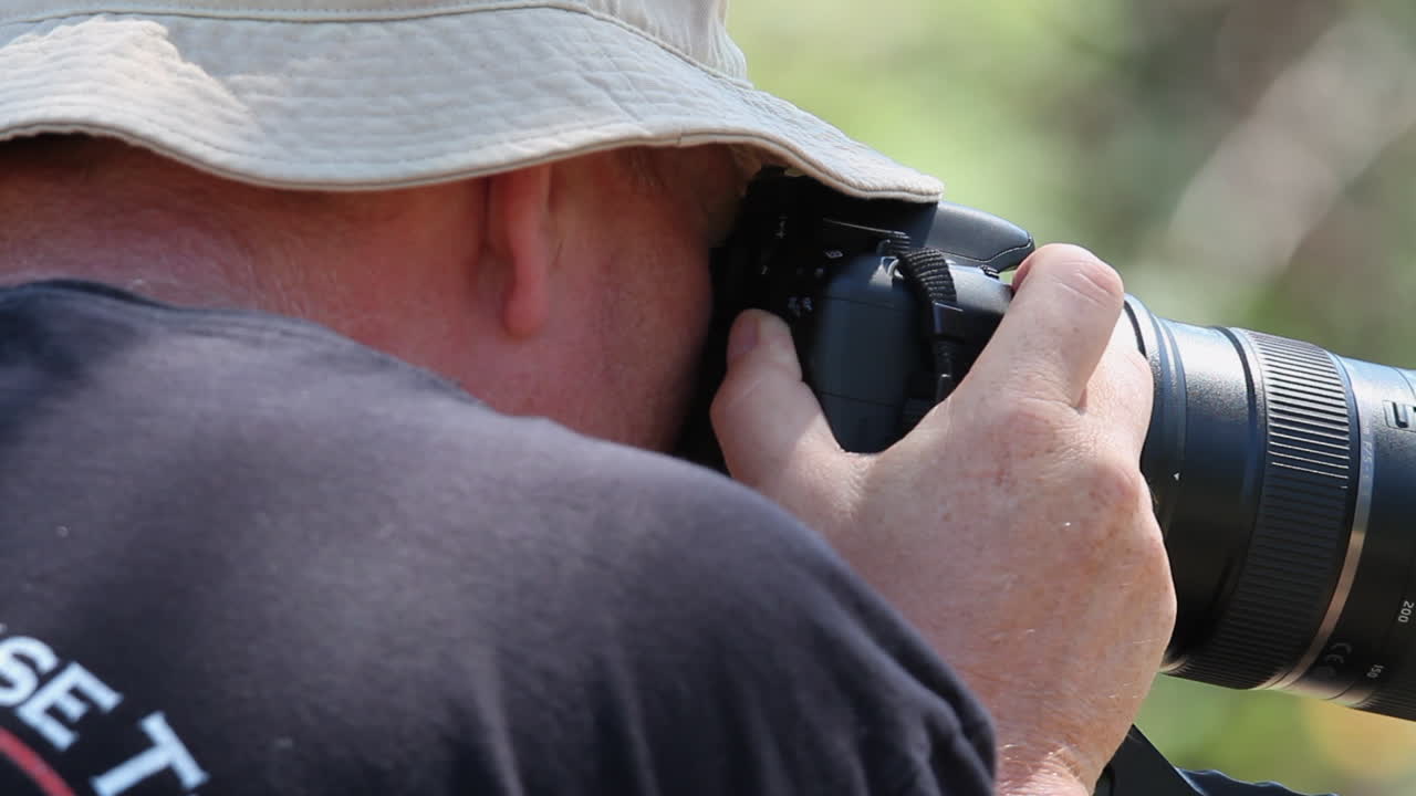 fotógrafo con sombrero con cámara y lente de zoom en los botones de ajuste del trípode