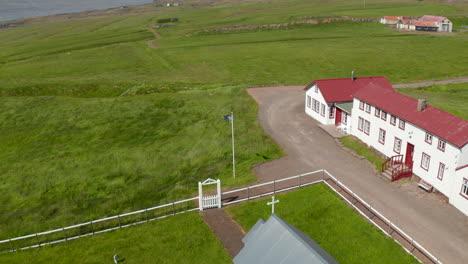 Birds-Eye-Drohne-Fliegt-über-Island-Fahnenschwingen-Im-Hochland.-Luftaufnahme-Der-Flagge-Von-Island,-Die-Im-Wind-über-Küstenpanorama-Mit-Felsigen-Bergen-Flattert