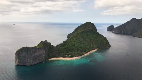 aerial view of duiklocatie helicopter island, philippines, revealing a pristine beach, turquoise waters, anchored boats, and dense forested hills surrounded by calm tropical sea