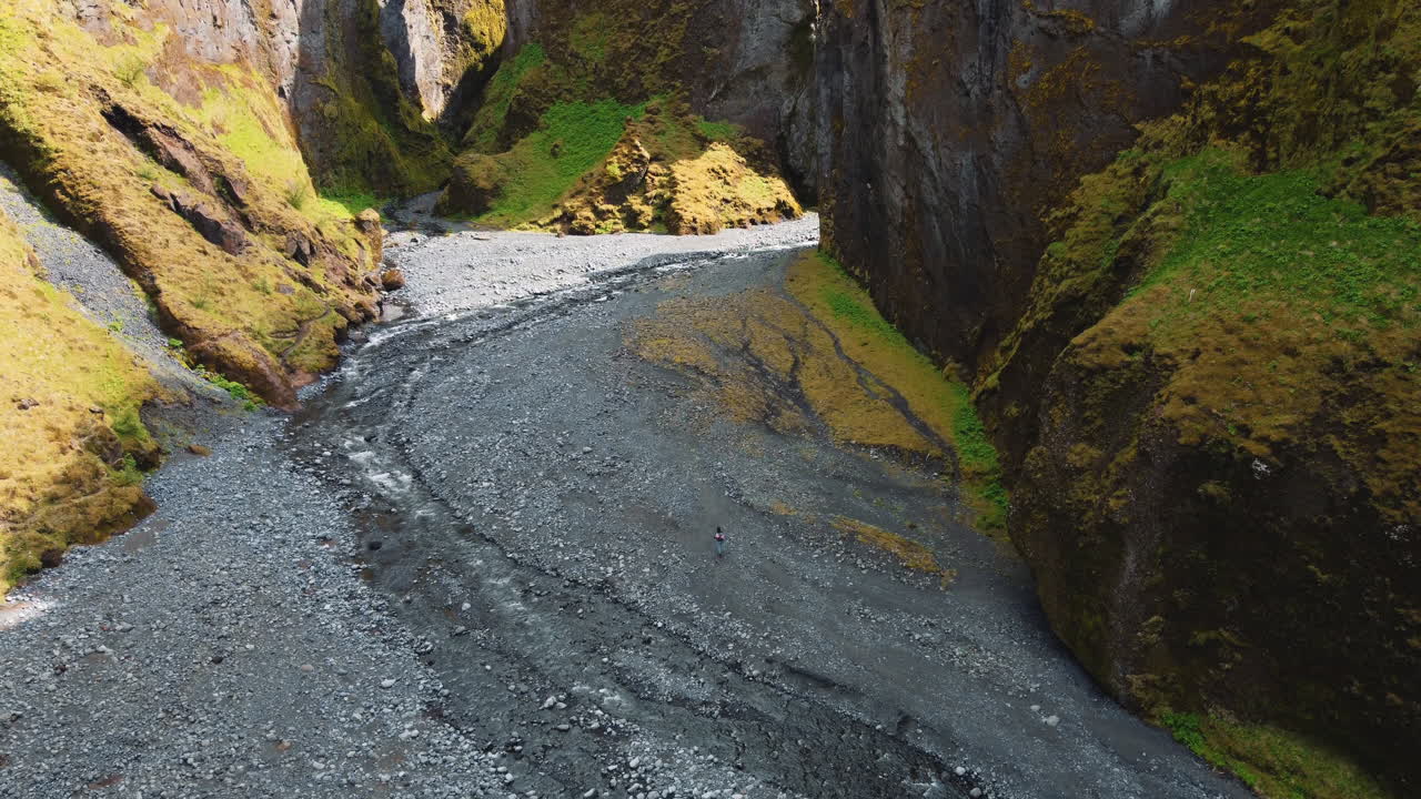 la vista aérea de un excursionista caminando sobre piedras en el fondo de un barranco con acantilados escarpados