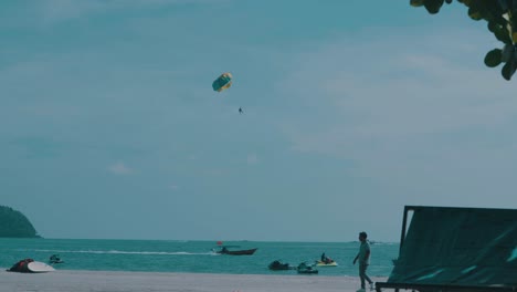 tourists enjoying a sunny day at the beach, parasailing and riding jet skis in the beautiful turquoise waters of langkawi, malaysia, a popular travel destination in southeast asia