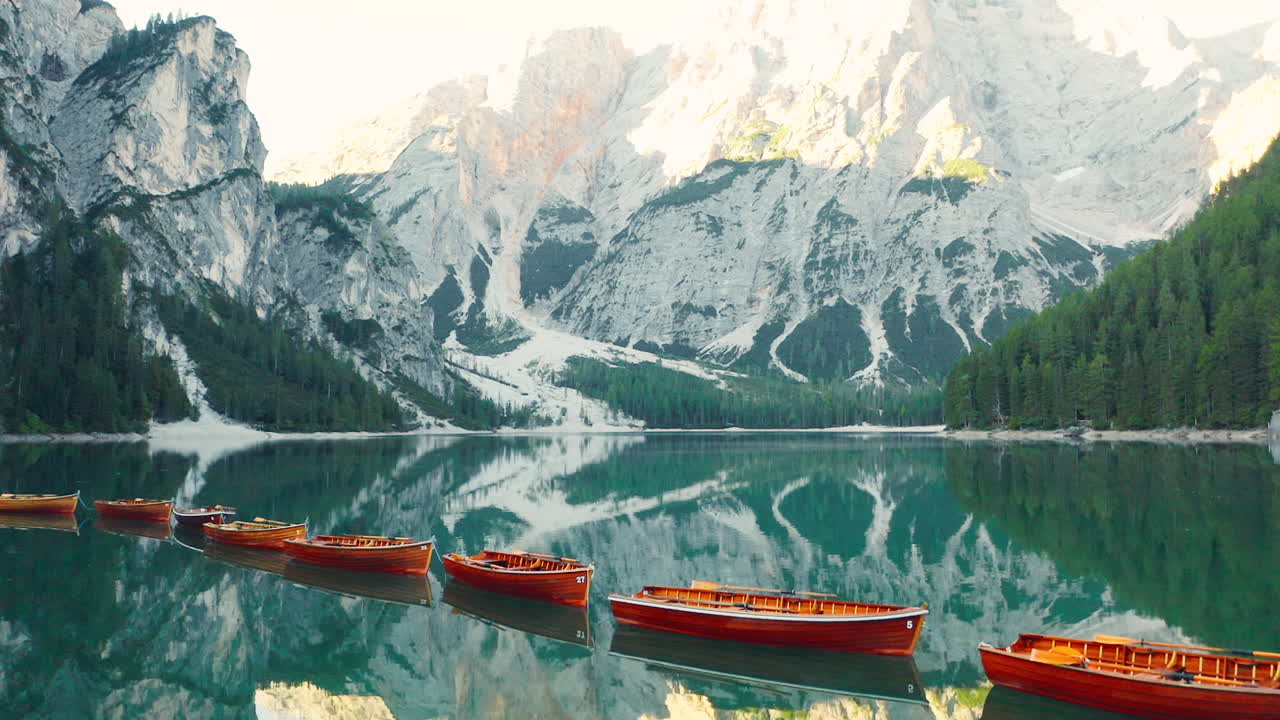 İtalya'daki Braies Gölü'nde Prags Dolomitleri'nin çarpıcı yansımaları ve sıralı kırmızı ahşap sandallar, havadan çekim.