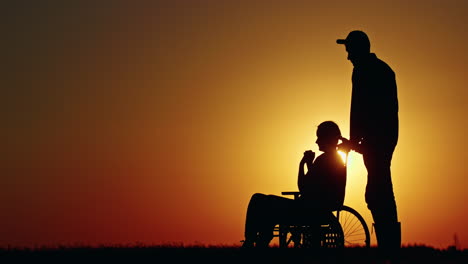 sunset silhouette of a caregiver and person in wheelchair