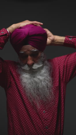 vertical video low key studio lighting shot of senior sikh man with beard tying fabric for turban against dark background 5