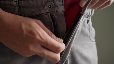 person, struggling slightly, zips up the mid-rise jeans, showcasing grey denim