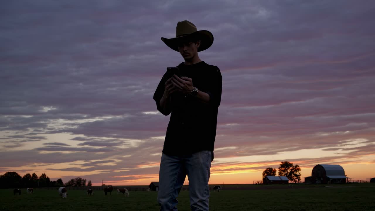 Cowboy using smartphone at sunset on a ranch