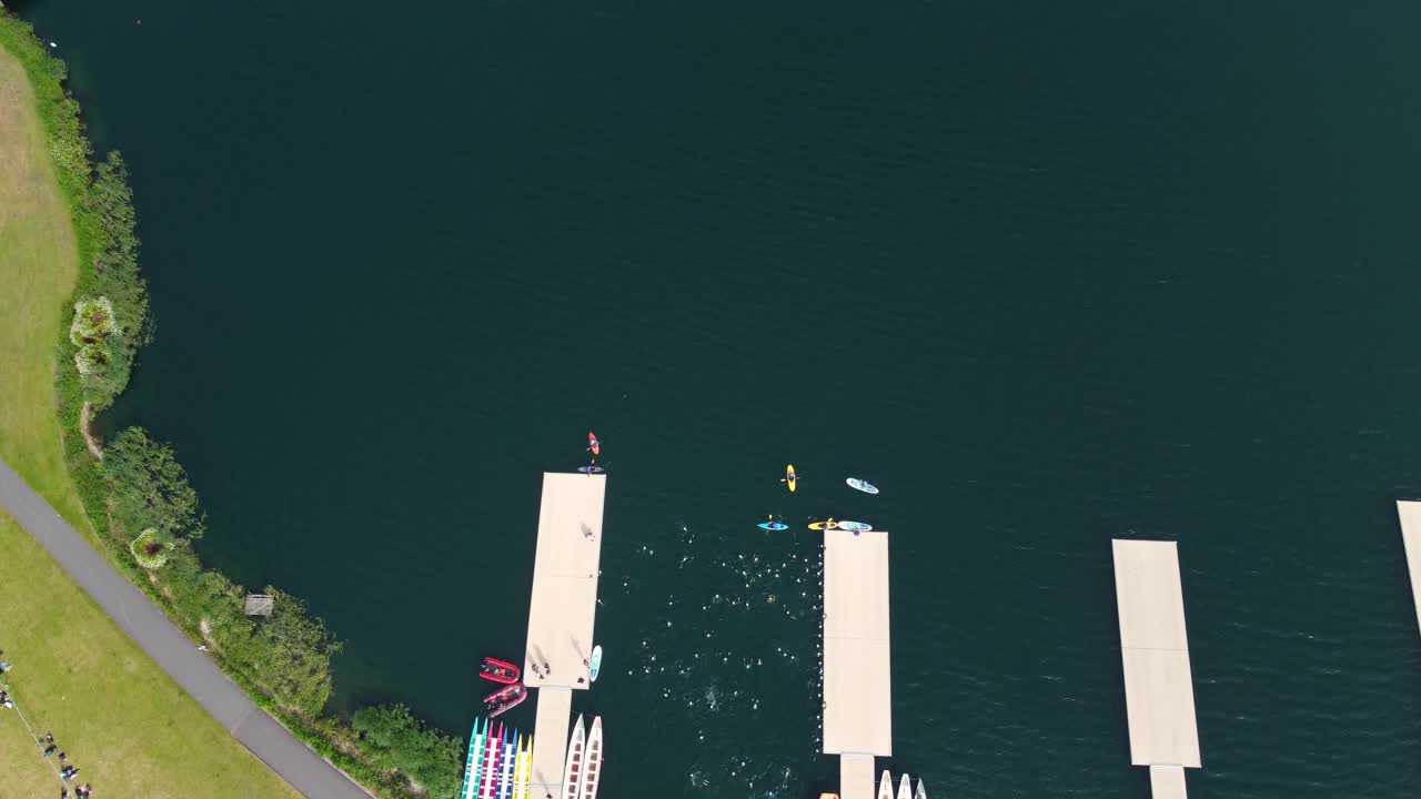 도르니 호수에서 트라이애슬론의 상단 각도, 트라이아슬론 선수들이 트랙에서 달리고 전환 지역으로 헤엄치고 있습니다.