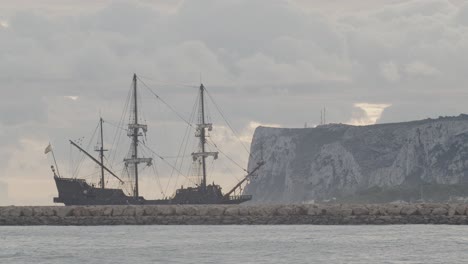 16th century galleon andalucia replica ship arriving at port in a cloudy day at sunrise behind a breakwater with mountain in the background