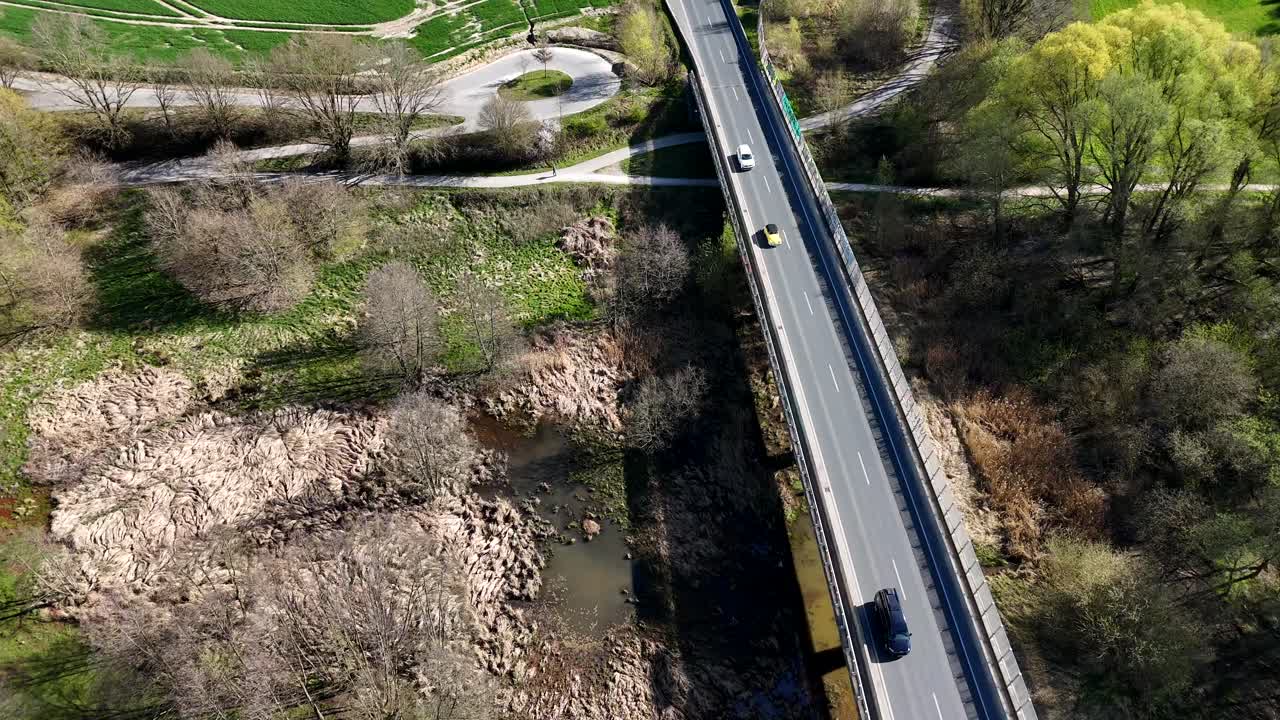 Traffic on newly built american interstate road between farm fields in spring season. Aerial top down flyover shot. Asphalt highway in Virginia, America. Dried out river lake after heat.