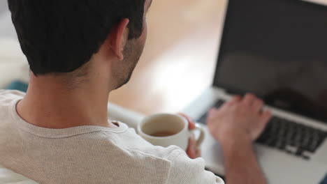 hombre bebiendo café mientras usa una computadora portátil