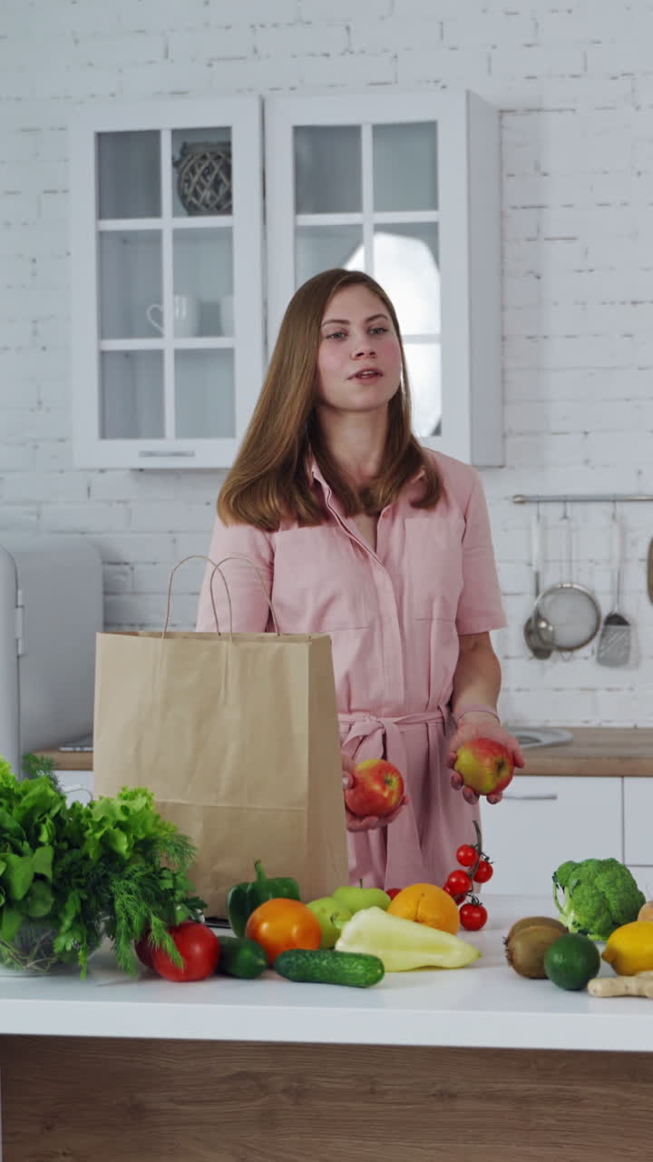 Healthy food on a kitchen table. Beautiful woman taking out fresh apples from shopping bag. Loving mom cares about nutrition. Vertical video