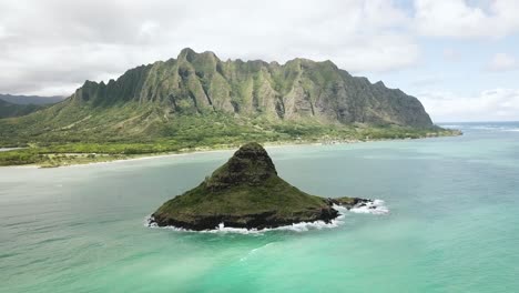 disparo de drones acercándose a la isla del sombrero de chinaman con el rancho de kualoa y la cordillera de kualoa en el fondo