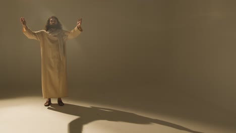 retrato de estudio de longitud completa de un hombre vestido con túnicas y sandalias con cabello largo y barba que representa la figura de jesucristo con los brazos extendidos