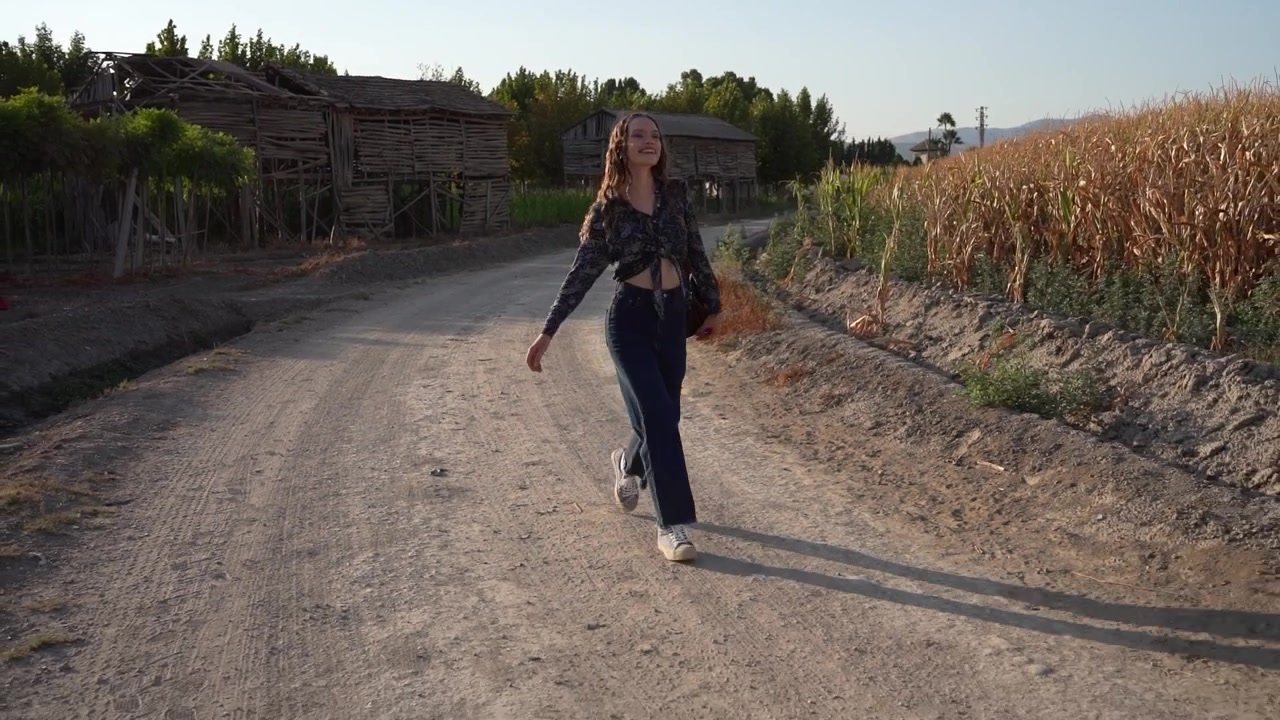 Una giovane donna cammina lungo una strada di campagna circondata da una natura splendida e vegetazione.