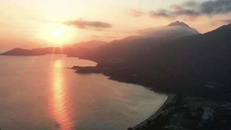 camión aéreo a la izquierda del mar y la bahía de la playa de pui o cerca del pueblo y las colinas de la selva tropical a la hora dorada con rayos de sol, la isla de lantau, hong kong, china