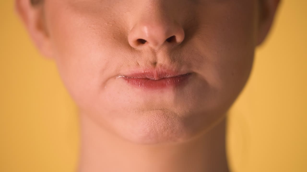 Extreme close up of woman lips making skeptical or superior gestures with her lip and puffing her cheeks against a yellow background in slow motion