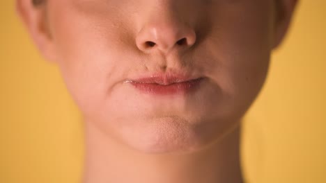 Extreme-Nahaufnahme-Der-Lippen-Einer-Frau,-Die-Mit-Ihrer-Lippe-Skeptische-Oder-überlegene-Gesten-Macht-Und-Ihre-Wangen-Vor-Einem-Gelben-Hintergrund-In-Zeitlupe-Aufbläht