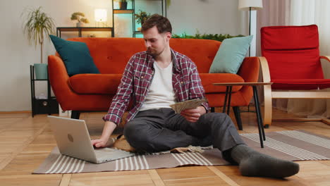 rich happy caucasian man counting money cash dollar using laptop calculate domestic bills at home